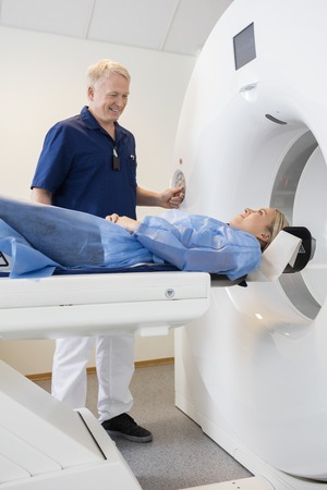 Smiling male professional looking at patient undergoing CT scan in hospitalの写真素材