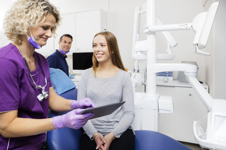 Assistant showing report to smiling young patient on digital tablet in dentistryの写真素材