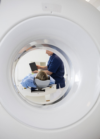 Doctor Showing Digital Tablet To Patient Seen Through CT Scannerの写真素材