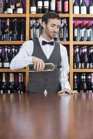 Young male bartender pouring white wine in glass at counterの写真素材