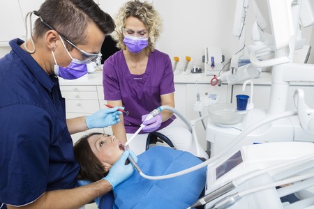 Mid adult male dentist with female assistant examining patient in clinicの写真素材
