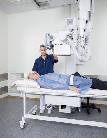 Young female doctor adjusting xray machine over male patient in hospitalの写真素材