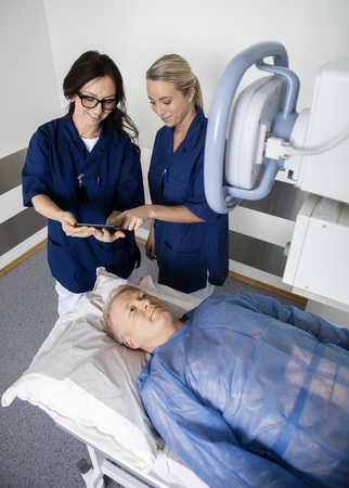 Radiologists Using Tablet Computer While Man Lying Under Xray Maの写真素材