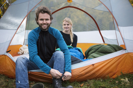 Man Tying Shoelace While Woman Relaxing In Tentの写真素材