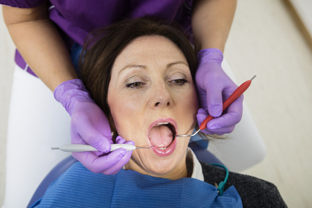 Patient With Mouth Open Being Examined By Dentist Holding Toolsの写真素材