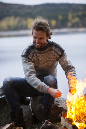 Man Warming Hands By Bonfire On Lakeside Campingの写真素材