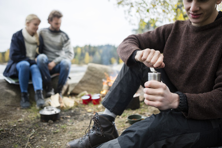 Man Grinding Coffee With Friends At Campsiteの写真素材