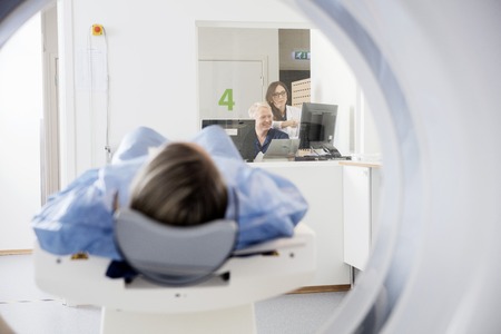 Doctors Using Computers While Patient Undergoing CT Scan