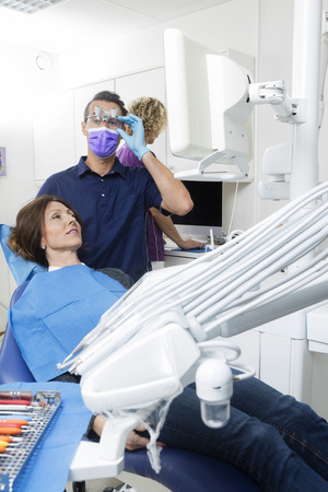 Male Dentist Examining Patient While Assistant Working At Dentisの写真素材