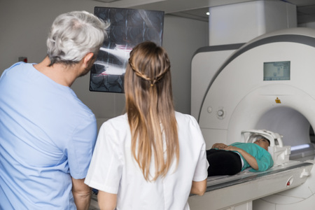 Doctors Analyzing X-ray With Patient Lying On CT Scan Machineの写真素材