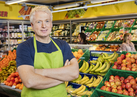 Smiling Salesman Standing Arms Crossed By Fruits In Storeの写真素材