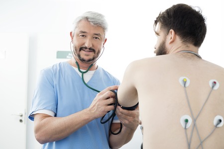 Portrait Of Doctor Measuring Blood Pressure Of Patient In Hospitの写真素材