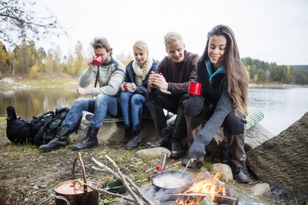 Woman Cooking Food On Campfire With Friends In Backgroundの写真素材