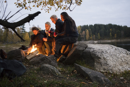 Young Friends Relaxing By Campfire On Lakeshoreの写真素材