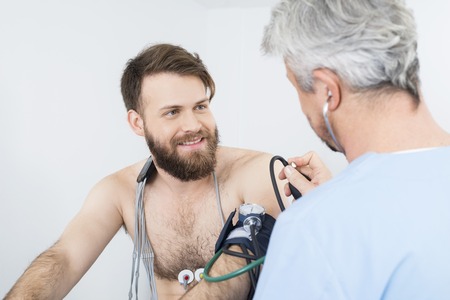 Patient Looking At Doctor Checking Blood Pressureの写真素材