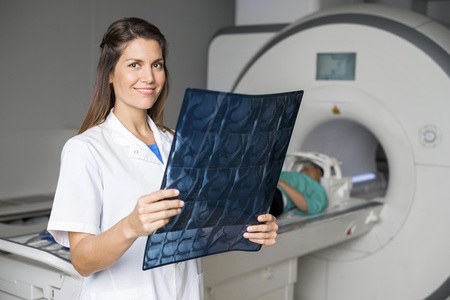 Doctor Holding X-ray While Patient Lying On CT Scan Machineの写真素材