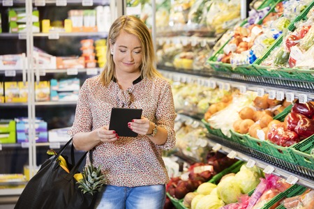 Customer Using Digital Tablet While Shopping In Grocery Storeの写真素材