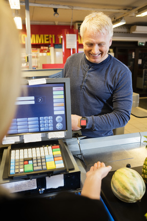 Customer Paying Through Smartwatch While Female Cashier Guidingの写真素材