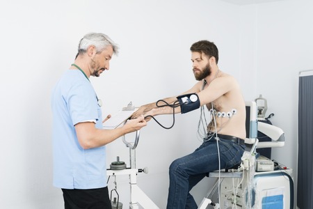 Doctor Checking Blood Pressure Of Patient Sitting On Exercise Biの写真素材