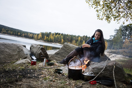 Young Woman Sitting Near Campfire On Lakeshoreの写真素材