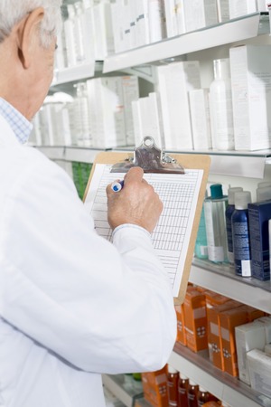 Pharmacist Writing On Clipboard While Counting Stock In Pharmacyの写真素材
