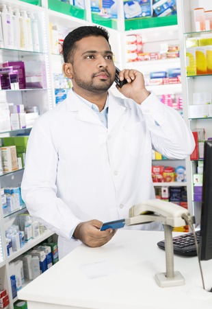 Confident Pharmacist Using Phone While Holding Credit Cardの写真素材