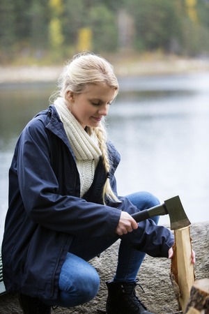Woman Cutting Wood For Bonfire On Lakeside Campingの写真素材