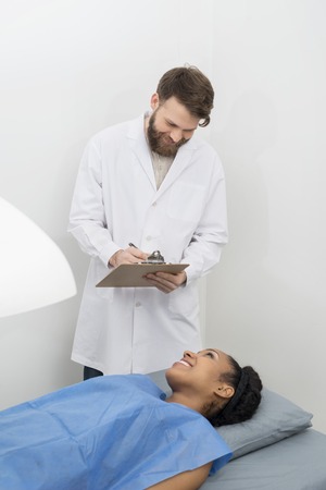 Doctor Writing On Clipboard While Patient Undergoing Bone Densitの写真素材