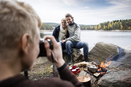 Man Photographing Couple At Lakeside Campingの写真素材