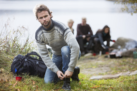 Hiking Male Tying Shoelace With Friends In Backgroundの写真素材