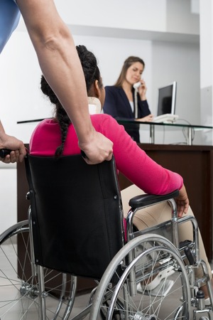 Doctor Pushing Patient On Wheelchair While Receptionist Workingの写真素材