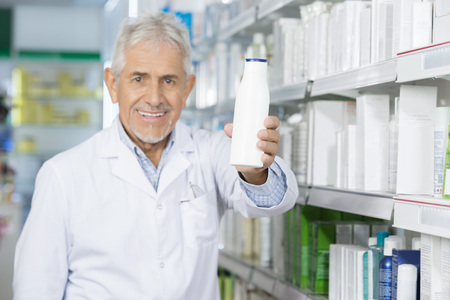 Smiling Pharmacist Holding Shampoo Bottle In Pharmacyの写真素材