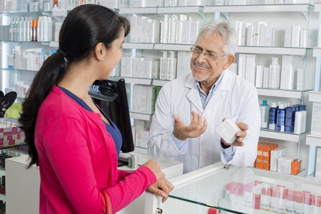 Chemist Gesturing While Communicating With Female Customerの写真素材