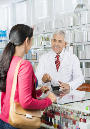 Chemist Swiping Card While Looking At Customer In Pharmacyの写真素材