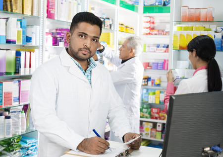 Confident Chemist Writing On Clipboard While Colleagues Workingの写真素材