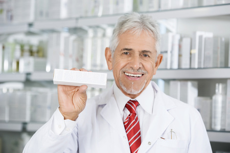 Smiling Pharmacist Holding Medicine Box Against Shelvesの写真素材