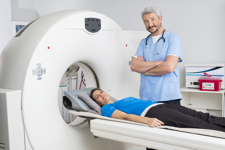 Doctor Standing Arms Crossed By Patient Lying On MRI Machineの写真素材