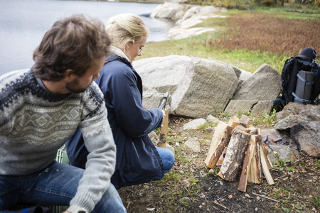 Man Looking At Woman Chopping Wood On Campsiteの写真素材