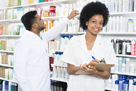 Pharmacist Writing On Clipboard While Colleague Arranging Producの写真素材