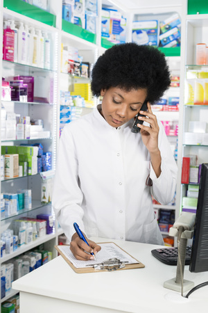 Pharmacist Writing On Clipboard While Using Cordless Phoneの写真素材