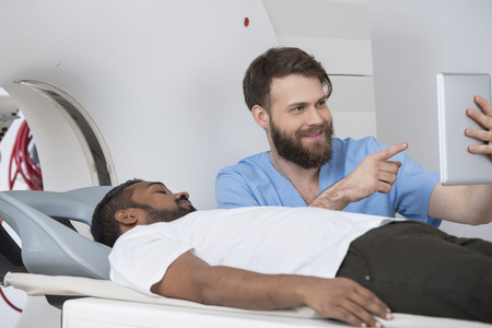 Doctor Showing Digital Tablet To Patient Lying On CT Scannerの写真素材