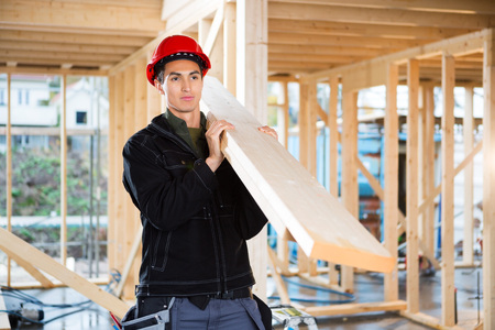 Carpenter Carrying Wood While Looking Away At Construction Site