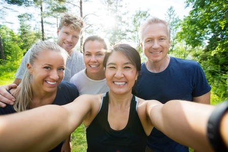 Portrait of happy mature woman taking selfie with friends in forestの写真素材