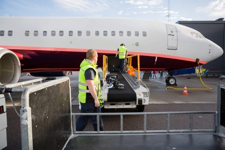 Crew Working At Luggage Conveyor Attached To Airplaneの写真素材