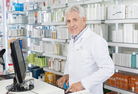 Senior Chemist Using Computer At Counter In Pharmacyの写真素材