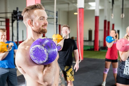 Male Instructor Lifting Kettlebell With Clients In Gymの写真素材
