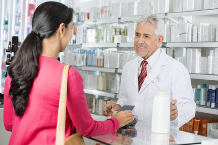 Pharmacist Looking At Female Making NFC Payment For Shampooの写真素材