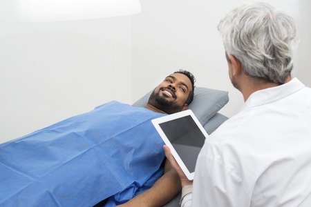 Patient On Bed Looking At Doctor Using Digital Tabletの写真素材