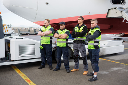 Confident Ground Team Standing Arms Crossed Against Airplaneの写真素材
