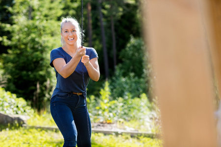 Smiling Young Woman Pulling Rope Attached To Wooden Structure